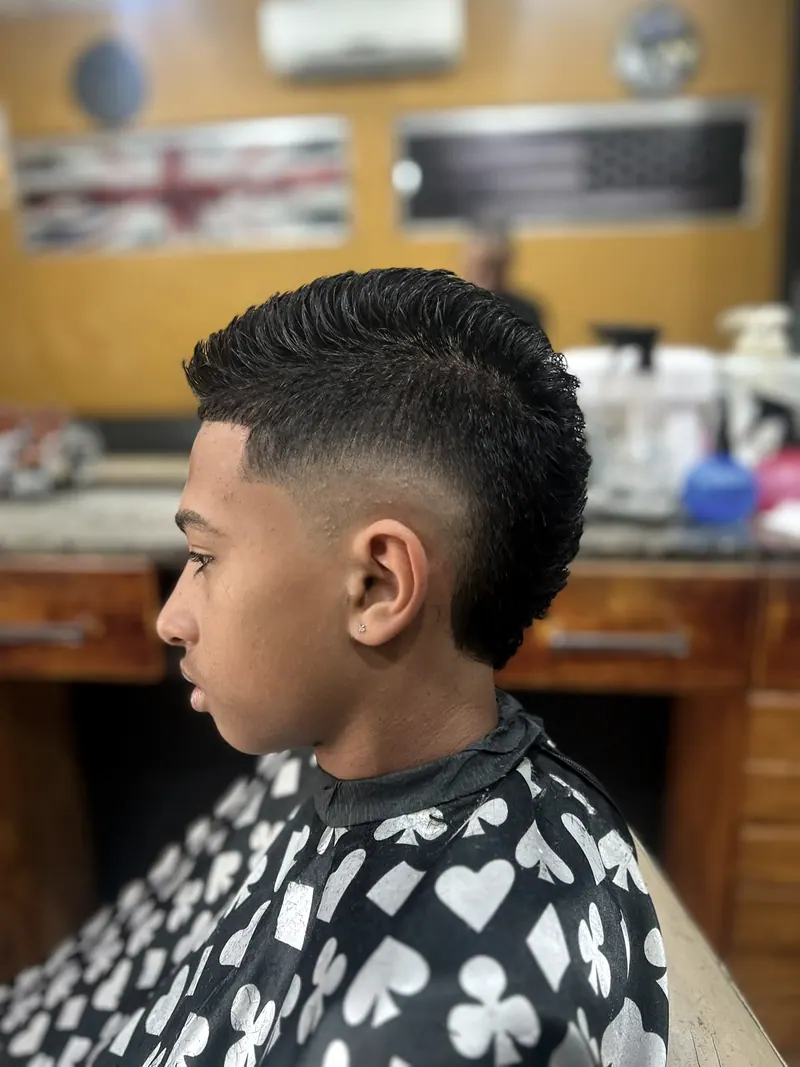 Moicano com degradê em menino, de perfil, na barbearia de parede amarela