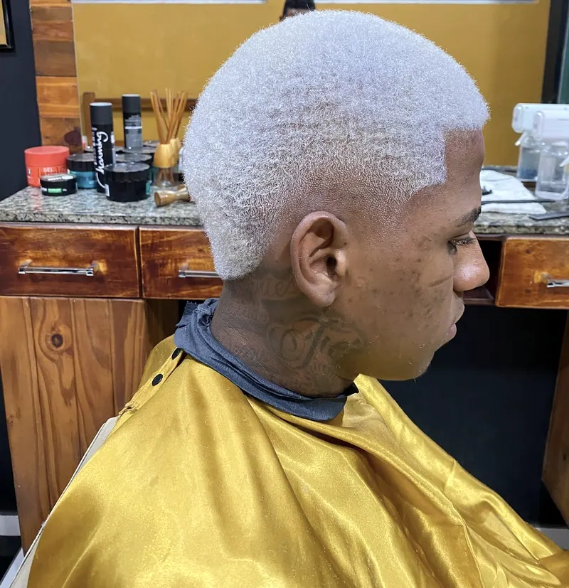 Corte platinado com degradê, de perfil, na barbearia de parede amarela